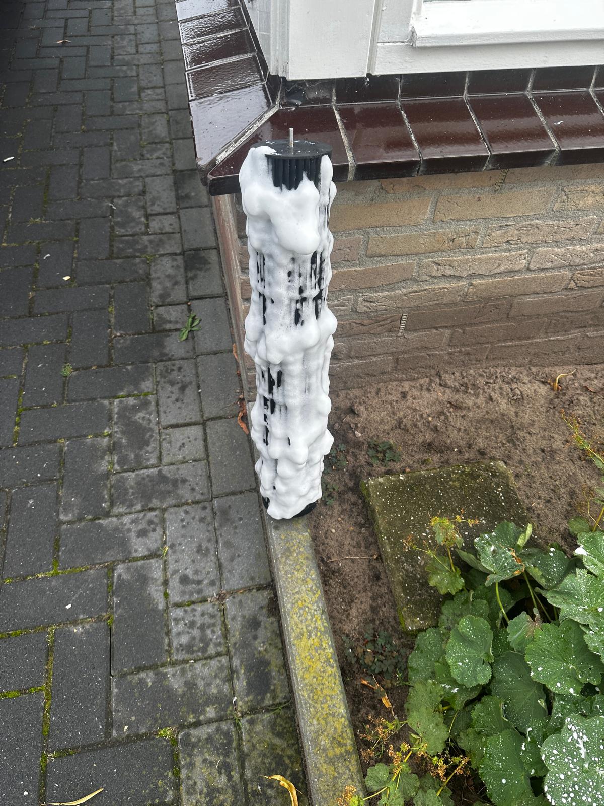 Uitgebouwde ventilatorrol van een airco onder wit reinigingsschuim, met zwart vuil dat eruit loopt