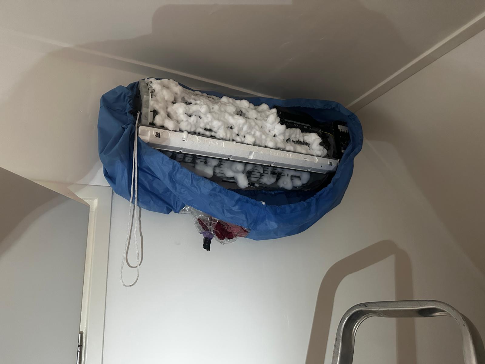 Witte schuimreiniging op de verdamper van de airco binnenunit binnen de servicezak — het vuil wordt losgeweekt